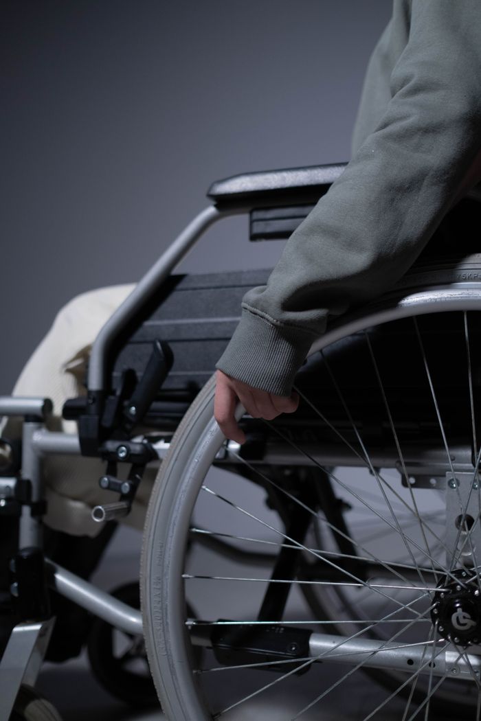 A detailed close-up shows a person's hand resting on a wheelchair rim, emphasizing disability and mobility aids.