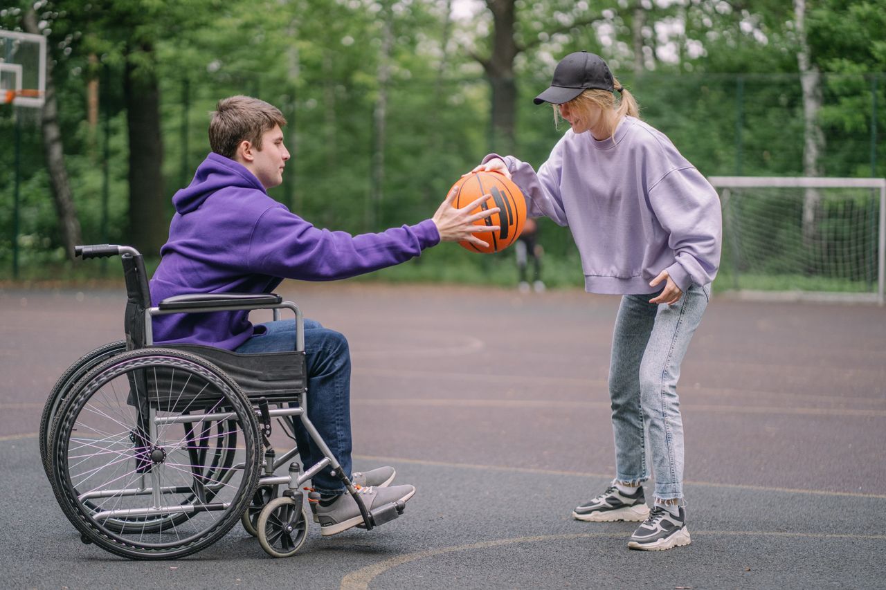 A young man in a wheelchair and a woman enjoying basketball outdoors, promoting inclusivity.
